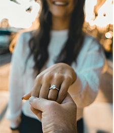 Man holding girlfriend's hand and showing diamond engagement ring on her finger